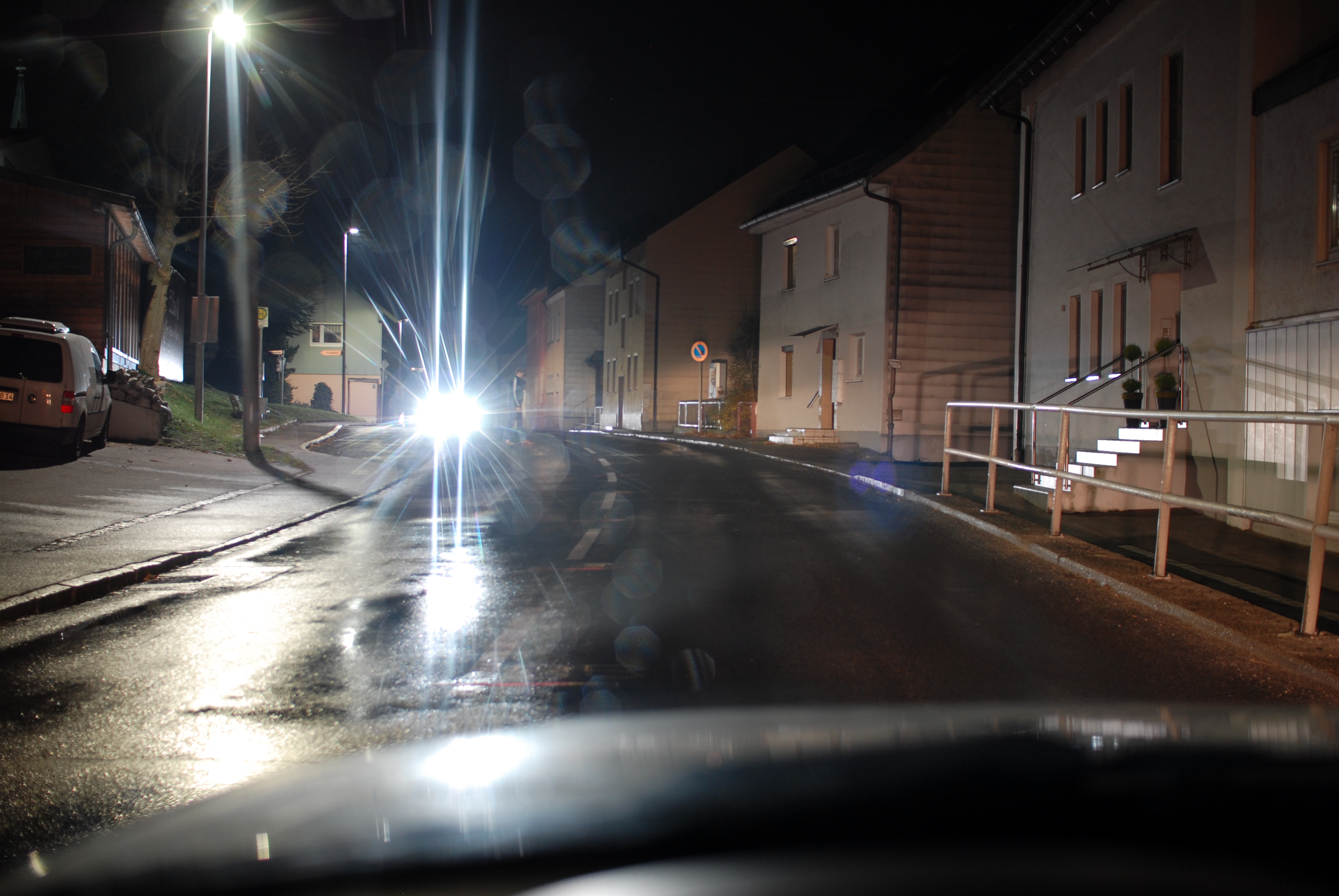 Sicht auf einen dunkel gekleideten Fußgänger mit Blendung durch den Gegenverkehr beim Überfahren einer Kuppe